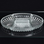 VIDRO, uma (1) petisqueira oval, incolor e translúcida, em quatro módulos, modeladas em sulcos, medindo unidas 31,5 x 19,5 cm, um dos módulos com bicadinho na borda, sinais de uso, vide foto.