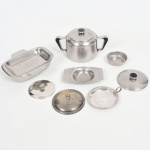 AÇO INOX METAL PRATEADO, nove (9) itens: 1 açucareiro com tampa, manufatura WOLFF (tradição desde 1894); 1 coador individual da marca HÉRCULES; 1 manteigueira, marca MERIDIONAL; 3 tampas descasadas; 1 covilhete pequeno circular; 1 palmatória com borda canelada, fundo com elementos vegetalistas em baixo relevo, todos os itens com sinais de uso, vide foto.