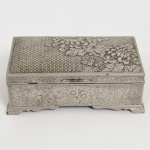 METAL PRATEADO, uma (1) caixa retangular, ornamentação relevada em elementos vegetalistas, interior forrado em madeira, sem marca de manufatura aparente, medindo 15 x 9 x 5 cm, sinais de uso, vide foto.