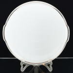 PORCELANA, um (1) medalhão para torta ou bolo, tonalidade branca, arremate com friso prateado, medindo 28 cm diâmetro mais as alças, modelo MEDAILLON, manufatura RENNER (Porto Alegre, RS, fundada em 1942; em 1998 foi vendida para a Vista Alegre de Portugal; em 1999 mudou a razão social para Vista Alegre do Brasil), sinais de uso, vide foto.