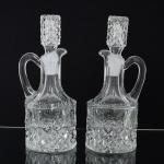 VIDRO, par (2) galhetas com alça e  tampa, incolores e translúcidas, modelagem em sulcos e geométricos, fundo floral, medindo 18,5 cm altura, sinais de uso, vide foto.