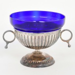 METAL PRATEADO, uma (1) pequena fruteira ou centro de mesa canelada e de pé baixo, alças circulares com detalhe macetado, marca BRISTOL, recipiente no formato de campanula na tonalidade azul e translúcido, medindo com recipiente 13,5 cm diâmetro e 11,5 cm altura, sinais de uso, vide foto.