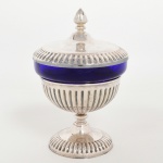 METAL PRATEADO, uma (1) pequena fruteira ou centro de mesa canelada, pé baixo e tampa com pega na forma de pinha, marca BRISTOL, recipiente no formato de campanula na tonalidade azul e translúcido, medindo 20,5 cm altura, sinais de uso, vide foto.