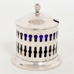 METAL PRATEADO, uma (1) molheira com tampa, cilíndrica, vazada em gradil, tampa encimada por pinha, marca SOPPIL, interior com recipiente em vidro na tonalidade azul e translúcido, medindo 11 cm altura e 10 cm diâmetro, sinais de uso, vide foto.