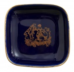 Porta alianças em pasta de porcelana francesa LIMOGES  Castel. Peça esmaltada em azul cobalto, formato quadrado, rica decoração dourada central com cena galante em estilo rococó e borda fileteada a ouro. Marca no verso Porcelaine Limoges Castel  Fabriquée et Décorée à Limoges. Mede 9 x 9 cm.