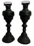 Par de antigas luminárias de mesa em metal patinado de tonalidade escura, ricamente trabalhados em relevo com motivos florais e arabescos. Peças de corpo torneado, base circular e bocal vazado com galeria perfurada, típicas de produção decorativa do final do século XIX / início do século XX. Conjunto decorativo de forte presença estética, ideal para ambientações clássicas ou colecionismo. Possui boca e fiação. Funcionamento desconhecido. Mede 50 cm altura.