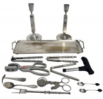 Conjunto com bandeja retangular em metal prateado, par de castiçais sendo um no estado e seleção de utensílios antigos em metal, incluindo pinças, alicates, colheres, espátulas e peças diversas, com pátina do tempo e sinais de uso compatíveis com a idade. Lote decorativo e colecionável. Total de 13 peças, medida da maior 38cm.