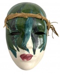 Máscara decorativa de parede, em porcelana esmaltada, representando face feminina estilizada, com pintura policromada em tons de verde, azul e lábios em vermelho. Peça com acabamento vitrificado e cordão lateral para fixação. Marcas do tempo. Mede 12cmX18cm.