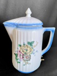 Ebulidor em porcelana esmaltada com decoração floral e detalhes azuis, base c/ resistência elétrica corpo e tampa c/ relevo canelado.