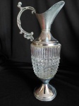 Ânfora em metal prateado com corpo em vidro trabalhado e bico translúcido. Alças trabalhadas em arabescos. Medidas: 35 cm de altura x 22 cm de diâmetro.