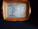 Bandeja com borda elevada em madeira com fundo em metal trabalhado em alto relêvo artesanalmente revestido com vidro. Pegas laterais. Alt. 6cm x 30cm x 23cm