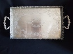 Bandeja retangular com alças espessurado a prata. Galeria vazada com volutas e rosaceas. Fundo lavrado e cinzelado com flores. Pés elevados. Medidas com alça - 46 x 24 cm x 7 cm altura