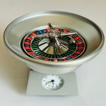 COLECIONISMO - Miniatura de relógio em formato de roleta de cassino em metal. Medindo Largura 8 x Altura 5 cm x Profundidade 4 cm.