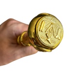 Bengala em madeira escurecida com castão dourado, formato tradicional com detalhes de símbolos maçônicos. Parte interna com estoque embutido.