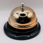 Campainha de mesa em metal e plástico duro, na cor bronze. Nova na embalagem.