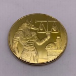 Moeda decorativa do Deus Egípcio Anúbis, feita em metal dourado, com case de acrílico. Diâmetro: 4 cm. Espessura: 0,3 cm. Anúbis é um Deus egípcio da vida após a morte. Como protetor das almas desamparadas, exerce a função de guiar os mortos às regiões celestes e auxiliar na sua ressurreição.