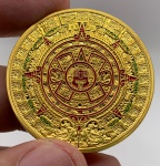 Moeda representando Calendário Maia em metal dourado com case de acrílico. Diâmetro: 4 cm. Espessura: 3 cm.