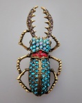 Broche em metal dourado representando Besouro todo trabalhado em pedrinhas, a cor predominante na peça é o azul e tons diversos . Medindo 7 x 3,5 cm.