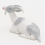 Pequena Escultura em porcelana, representando Bode, medindo 7 cm de altura por 10 cm de comprimento. Pequena falta no chifre.