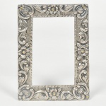 Grande Porta Retrato de prata, todo cinzelado com flores e volutas, forma retangular, medindo 16 cm por 12 cm. Peso bruto 112 g.