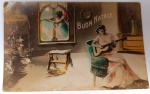 Antigo Cartão Postal Italiano "Buon Natale"  Alegoria Musical  Fotografia Colorizada à Mão (Circa 1910-1920)Raro cartão postal de Natal de origem italiana com uma composição rica em simbolismo. A imagem retrata uma cena de interior onde uma mulher toca um instrumento de cordas (violão/guitarra clássica), enquanto, através da janela, um anjo anunciador toca uma trombeta, simbolizando a boa nova do nascimento de Cristo.