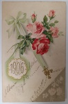 Antigo Cartão Postal "1906"  Cromolitografia com Relevo Dourado  Temática Floral (Rosas) e Manuscrito de ÉpocaRaríssimo exemplar de cartão postal de Ano Novo, datado de 1º de Janeiro de 1906. A peça é um exemplo clássico da estética da Belle Époque, unindo técnicas avançadas de impressão da época com a tradição de troca de votos manuscritos