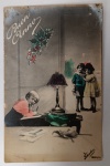 Antigo Cartão Postal Italiano "Buon Anno"  Temática Infantil e Escrita  Fotocromia (Circa 1910-1920)Belo cartão postal italiano de época, apresentando uma cena narrativa rica em detalhes. A imagem retrata uma criança escrevendo à luz de um candeeiro (simbolizando a mensagem de Ano Novo), enquanto outras duas crianças observam ao fundo. No topo, ramos de visco/azevinho, símbolo tradicional de sorte e proteção para o novo ano