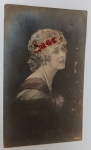 Antigo Cartão Postal Artístico  Retrato Feminino com Flores e Pérolas  Fotografia Colorizada à Mão (Circa 1900-1915)Magnífico retrato fotográfico de estúdio em formato de cartão postal. A imagem destaca a elegância feminina do início do século XX, com foco na iluminação dramática (estilo chiaroscuro) que ressalta a fisionomia e os ornamentos da modelo.