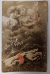 Antigo Cartão Postal Italiano "Buon Natale"  Menino Jesus e Anjos  Fotografia Colorizada (Circa 1910-1920)Cartão postal original de época, celebrando o Natal através de uma composição lírica. A imagem retrata o Menino Jesus deitado na palha, sob a vigilância de dois anjos que surgem entre nuvens, simbolizando a proteção divina e a celebração celestial do nascimento de Cristo.