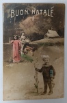Antigo Cartão Postal Italiano de Natal "Buon Natale"  Início do Séc. XXBelíssima cena litográfica retratando o Menino Jesus em um jumento, guiado por uma jovem em trajes de época. Em primeiro plano, um garoto segura flores secas e um pequeno embrulho azul. Ao fundo, paisagem invernal com chalé sob a neve