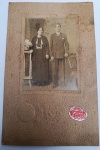 Fotografia Antiga - Retrato de Casal - Estúdio Photo Risat - Circa 1920/30 Retrato de corpo inteiro de um casal em traje formal, montado em cartão rígido original com moldura em relevo e textura "casca de ovo". Destaca-se o selo de autenticidade do estúdio em papel gomado vermelho no canto inferior direito.