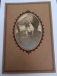 Fotografia Antiga - Retrato de Filhote (Pet Vintage) - Circa 1910-1920Rara e cativante fotografia de época retratando um pequeno cão (filhote) posicionado sobre uma cadeira de palhinha clássica. A imagem está montada em um cartão rígido original de cor parda, com uma moldura oval interna de acabamento denteado em relevo.