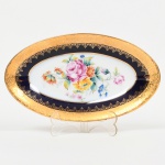 PORCELANA FRANCESA, um (1) covilhete oval com ornamentação floral policromada pintada a mão, faixa na tonalidade azul cobalto, generosos arremates a ouro, marca F.M  Porcelaine Artistique  LIMOGES  France, modelo LOURDES, medindo 23 x 13 cm, sinais de uso, vide foto.