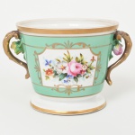 PORCELANA PORTUGUESA, um (1) cachepô com ornamentação floral pintada a mão, arremates a ouro, alças relevadas em rosas e galhos, marca VISTA ALEGRE (fundada em 1824, pelo negociante, lavrador, industrial e político, José Ferreira Pinto Basto, através de alvará concedido por D. João VI, tendo seu fundador associado a fábrica os seus 15 filhos, ficando a sociedade denominada Ferreira Pinto & Filhos; cinco anos mais tarde recebe o título real pelo reconhecimento de sua arte e sucesso, ficando conhecida como Real Fábrica da Vista Alegre, começou no fabrico de vidros enquanto se empenhava em esforços para a produção de porcelana, os primeiros ensaios conseguidos foram imperfeitos denominado loiça de pó de pedra, através de boas relações com a fábrica francesa de Sevres conseguiu as receitas para o fabrico de porcelana, somente em 1832, por sorte, é encontrado um jazigo de caulim situado em Aveiro, próximo a Ílhavo, a partir desta data o fabrico de porcelana foi se aperfeiçoando em Portugal, 1851 expôs com sucesso no Palácio de Cristal em Londres; 1852 D. Fernando II visita a fábrica e encomenda uma baixela completa; 1867 recebeu sua primeira premiação na Exposição Universal de Paris; 1880 interrompe a produção de vidros para se dedicar exclusivamente a porcelana; 1964 inauguração do Museu Histórico da Vista Alegre; ainda em funcionamento), medindo 11,5 cm altura e 14 cm diâmetro mais as alças, vide foto.