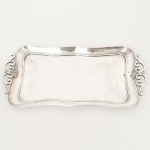 METAL PRATEADO, uma (1) bandeja bilheteira retangular, alças relevadas em volutas, medindo 26 x 13,5 cm até a alça, manufatura EBERLE (Abramo Eberle 1880, Monte Magrè 1945, Caxias do Sul, veio com uma das primeiras levas de imigrantes italianos para o Brasil em 1884 junto com seus pais Giuzeppe Eberle e Luigia Zanrosso, seu pai abriu uma pequena funilaria mas como tinha que trabalhar na lavoura quem cuidava era a mãe e o pequeno Abramo ajudava na funilaria; em 1896 quando o pai resolveu vender a funilaria para concentrar os esforços da família na lavoura Abramo, com 16 anos de idade, se propôs a comprá-la do pai, em 1918 já com o nome Abramo Eberle & Cia iniciou a fabricação de talheres e utensílios de mesa, morreu em 1945 com 65 anos de idade e os filhos deram continuidade aos negócios até 1984 quando venderam para o Grupo Zivi), sinais de uso, vide foto.