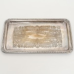 METAL PRATEADO, uma (1) bandeja,  fundo com ornamentação em baixo relevo representando volutas e elementos vegetalistas, borda relevada em corda, conchas e elementos vegetalistas, medindo 36 x 20 cm, sinais de uso, vide foto.