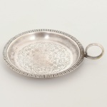 METAL PRATEADO, uma (1) palmatória com borda serrilhada, fundo ornado com flores em baixo relevo, alça curvilínea, medindo 8,5 cm diâmetro mais a alça, sem marca de manufatura aparente, sinais de uso, vide foto.