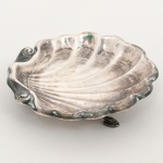 PRATA PORTUGUESA, um (1) porta aliança no formato de concha bivalve, pés em sapata com terminações em folhas, punções: águia e da marca de ourives não identificado, medindo 8 x 8 cm, peso aproximado 27,6 gr., sinais de uso, vide foto.