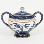 FAIANÇA JAPONESA, um (1) açucareiro com tampa, ornamentação WILLON (Segundo a lenda chinesa: Um certo Mandarim tinha uma leal e devotada filha, possuidora de rara beleza. Certo dia, em que descobre que ela estava apaixonada por um carteiro que lhe fazia a corte, e que era por ela correspondida, expulsa a filha de casa e roga-lhe uma praga: que ao ser trocado o primeiro beijo pelo casal, eles se transformariam em dois pombos), também conhecida como pombinhos, tonalidade azul sobre fundo branco, arremates a ouro, possui manchas e o craquejado característico do envelhecimento de toda a faiança, marca N. K. T. - Imperial Ironstoneware, Made in Japan, medindo 11 cm altura, sinais de uso, vide foto.