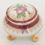 PORCELANA, uma (1) caixa com tampa, ornamentação floral policromada, faixas na tonalidade magenta, arremates a ouro, base trípode, sem marca de manufatura aparente, resquícios de cera na parte interna da tampa, medindo 7,5 cm altura, ideal para coleção de cristaleira, vide foto.