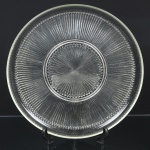 VIDRO, um (1) prato para torta ou bolo, incolor e translúcido, moldado em caneluras, marca representada pela letra B dentro de um escudo, bicadinhos na borda, medindo 33 cm diâmetro, sinais de uso, vide foto.