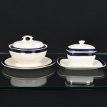 FAIANÇA INGLESA, dois (2) itens, ornados com faixa na tonalidade azul cobalto e arremates a ouro: 1 manteigueira com tampa e presentoir acoplado, marca THOMAS HUGHES, (Thomas Hughes Ironstone China, estabelecido de 1860 a 1876, Waterloo Road, Burslem; de 1872 a 1894, Top Bridge Works, Longport, Burslem; em 1895 virou Thomas Hughes & Son; em 1910 acrescentou no nome a palavra Ltd, funcionou até 1957), medindo 14,5 cm; 1 molheira com presentoir acoplado, marca WOOD & SONS (fundada em 1865, funcionou na Potteries New Wharf em Trent e mais tarde na Pottery Stanley em Burlem, fechou em 2005), medindo 13 x 9,5 x 7,5 cm, possuem o craquejado característico do envelhecimento de toda a faiança, manchas e sinais de uso, vide foto.