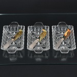 CRISTAL, três (3) petisqueiras moldadas em geométricos e sulcos, incolores e translúcidas, medindo 17,5 x 9,5 cm, acompanha 3 espátulas em aço inox com cabo em polímero colorido na forma de pássaro, sinais de uso, vide foto.