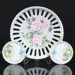 PORCELANA, três (3) itens: 1 prato com borda vazada, ornamentação pintada a mão com rosas em policromia, medindo 19,5 cm diâmetro, possui quebrados e colados na borda; 2 porta copos com ornamentação floral policromada, pintados a mão, Atelier YVETTE 1973, medindo 8,5 cm diâmetro, todos os itens da marca SCHMIDT (Pomerode, SC; Mauá, SP; Campo Largo, PR, fundada em 1945, ainda em atividade, maior fábrica de porcelana da América Latina), sinais de uso, vide foto.