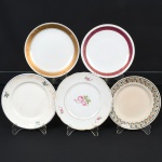 PORCELANA E FAIANÇA, cinco (5) pratos distintos: 1 ornado com rosas em policromia, frisos a ouro, marca REAL (Mauá, SP, 1943 a 1994), medindo 18,5 cm diâmetro; 1 com borda ornada em faixa dourada e silhuetas vegetalistas, marca STEATITA (Campo Largo, PR, funcionou de 1954 a 1994), medindo 19 cm diâmetro; 1 com borda ornada com faixa na tonalidade magenta, arremates a ouro, marca REAL, medindo 18,5 cm diâmetro; 1 ornado com flores em policromia, marca NADIR FIGUEIREDO (fundada em 1912 em São Paulo, como oficina para máquina de escrever; em 1943 comprou a fabrica de louça Santa Rita que ficou ativa até 1950; em 1944 comprou as fazendas Santa Terezinha e Fortaleza, onde construiu uma nova fábrica chamada Vila Operária que começou a operar em 1948; em 1947 iniciou a produção do copo de vidro americano; em 1955 iniciou a produção de copo para envase de requeijão; registrou as seguintes marcas: em 1956 a KOPAL; em 1957 a ROSICLER e PIREFRAX; em 1979 a KERAMIK; em 1982 a POTTERY; em 1992 a DURAMIK; em 1993 encerrou a produção de louça), medindo 18,5 cm diâmetro; 1 ornado com barrado em trigo, policromado, marca não identificada, medindo 18 cm diâmetro, todos com sinais de uso, vide foto.