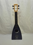 Antigo ukulele da The Magic Uke Company, New Hartford, Connecticut (EUA), com corpo em formato trapezoidal, acabamento azul escuro com decoração temática de lua crescente e estrelas, braço em madeira com escala escura marcada por pontos, quatro cordas, tarraxas pretas, etiqueta original visível no interior da boca e saída para captação elétrica instalada na lateral, indicando possibilidade de uso amplificado; apresenta desgaste natural do tempo, riscos superficiais e pátina compatíveis com a idade, sem quebras aparentes, mantendo bom apelo estético e colecionável. Medindo 19cm x 8cm x 57cm de comprimento.