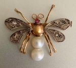 BROCHE EM OURO E PLATINA REPRESENTANDO ABELHA, COM PÉROLAS E RUBIS.Delicado broche em forma de abelha, confeccionado em ouro amarelo, com aplicação de platina nas asas, ricamente trabalhadas com gravação geométrica e pequenas incrustações de pedras claras, conferindo brilho sutil e textura refinada. O corpo apresenta acabamento polido, com olhos compostos por dois pequenos rubis de coloração viva, que trazem contraste e acento cromático à composição.O abdômen é formado por duas pérolas esféricas de tonalidade creme, com boa presença de nácar e brilho suave, criando equilíbrio entre o rigor do metal e a organicidade da matéria. Dimensões: 3,3 cm x 3 cm. Peso: 4,43 g.