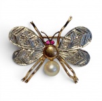 BROCHE EM FORMA DE ABELHA EM OURO E PLATINA, COM PÉROLA E RUBIS.  Delicado broche representando abelha, confeccionado em ouro amarelo, com aplicação de platina nas asas, finamente decoradas com gravação geométrica conferindo brilho discreto e elegante.O corpo apresenta acabamento polido, com olhos formados por dois rubis de tonalidade viva, que introduzem contraste cromático à composição.O abdômen é representado por uma pérola esférica de tonalidade creme, de brilho suave e nácar aparente, agregando equilíbrio entre a estrutura metálica e o elemento orgânico.Dimensões: 2,7 cm x 2,3 cmPeso: 3,87 g.