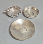 Três cinzeiros em Prata 900. Dois deles, decorados com moedas. Peso: 169 gramas. Med. 8 x 7 cm e 10 cm.
