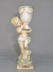 Antiga e grande escultura com floreira em biscuit europeu policromado, representando figura de criança segurando ânfora. Detalhes dourados. Altura 47 cm. Discreto restauro na quina da base.